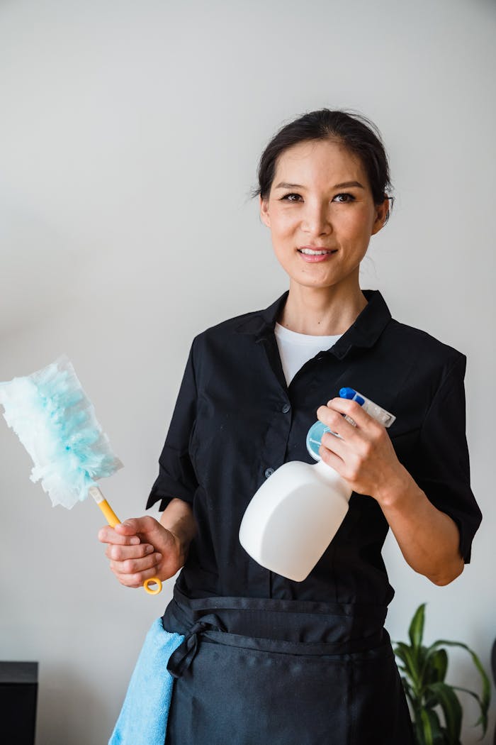 services-02 A female housekeeper smiling while holding cleaning tools indoor.